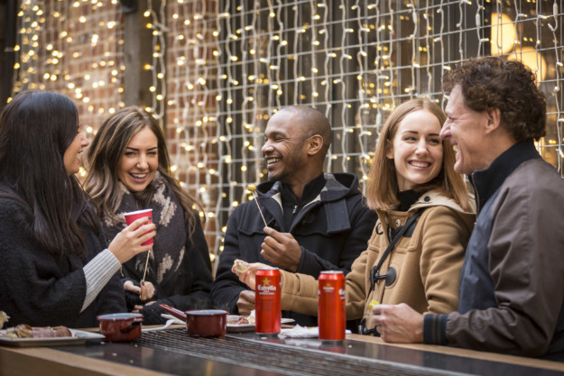 group of people share food and laugh in front of Christmas lights