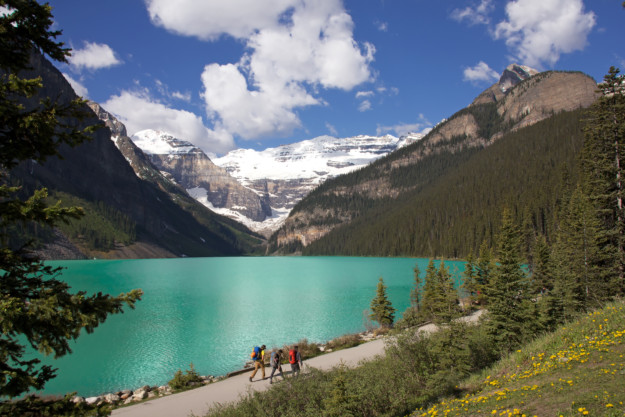 three hikers walk along the path alongside the turquoise waters of Lake Louise