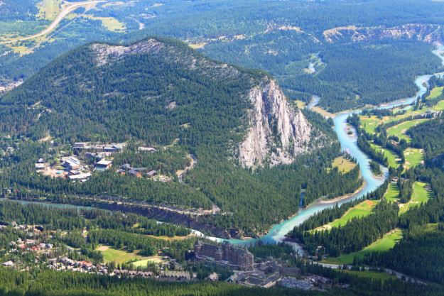 a bright turquoise river runs alongside a tree covered mountain with a sheer cliff face and the town of Jasper in the foreground