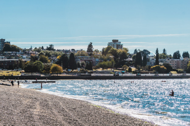 a man paddles on the sparkling ocean with a stony beach to the left