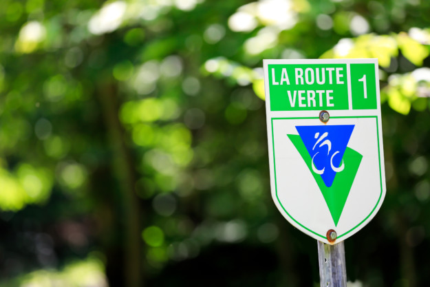 A green and white road sign reading "la route verte 1" with a bicycle symbol, positioned against a blurred forest background in Québec.