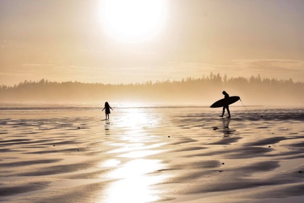 a surfer and a child walk along Tofino Beach