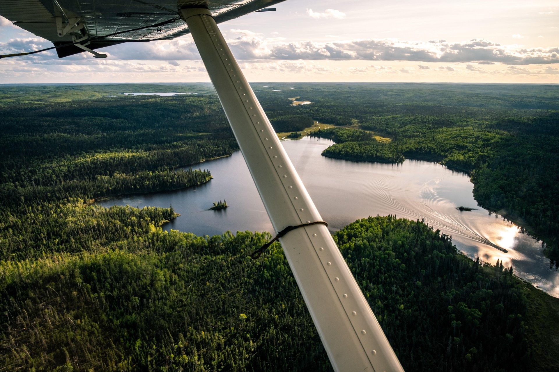 A view from a float plane flying over a lake encircled by lush-green boreal forest in Northern Saskatchewan 