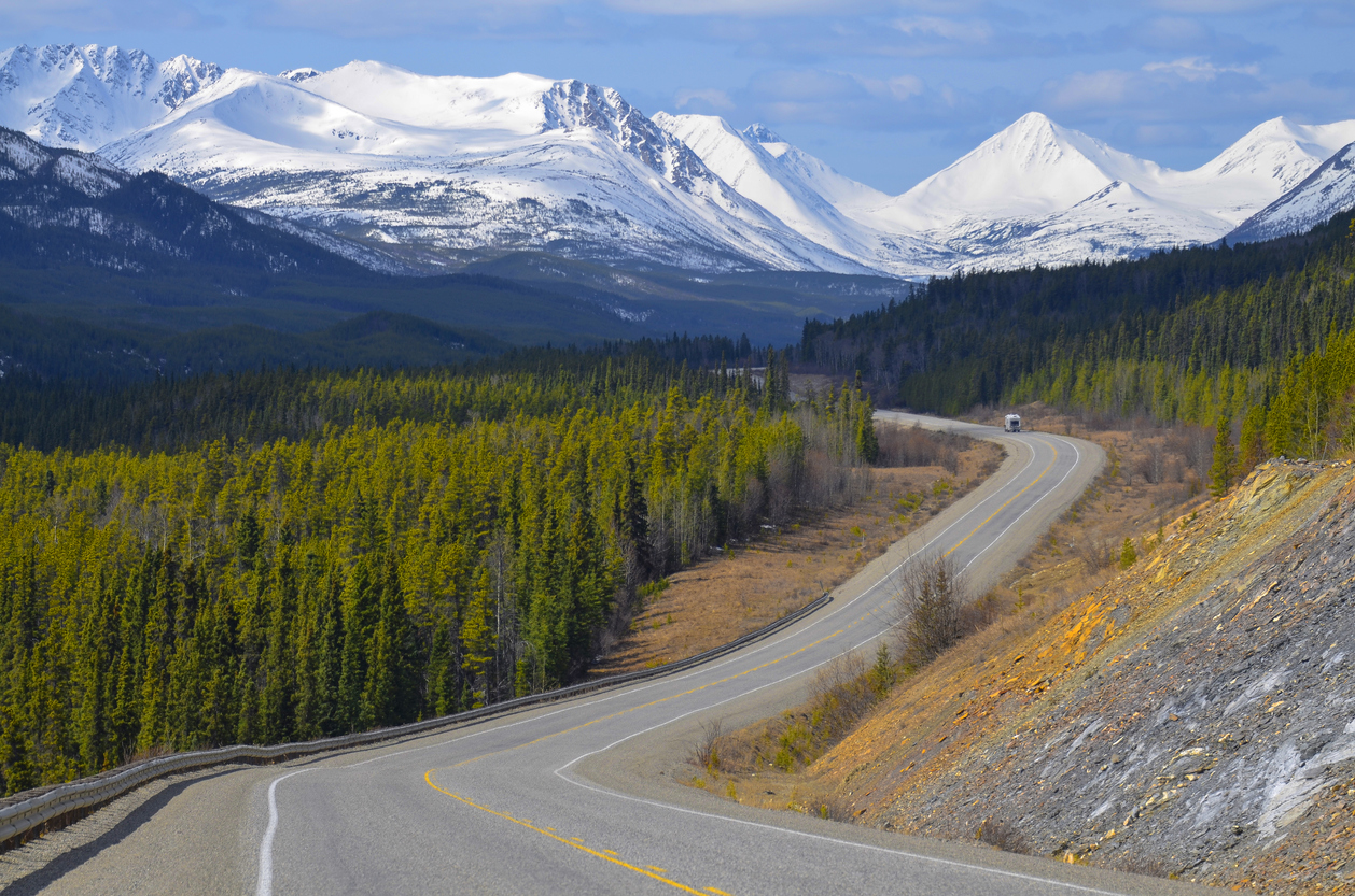 A scenic stretch of Alaska Highway in Yukon with snow-covered mountains on the background