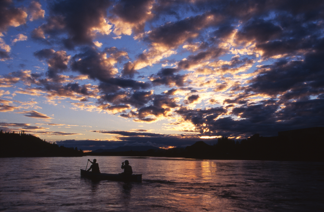 Two people canoeing on the Yukon River near Whitehorse with beautiful clouds and midnight sun overhead