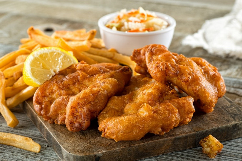 Golden fried fish fillets with crispy fries and coleslaw, served on a wooden board with a lemon wedge in Nova Scotia style.